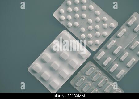 Tablets and capsules in pharmaceutical packaging arranged on a minimal grey-green background Stock Photo
