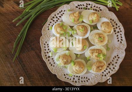Deviled eggs with cod livers with leek on white plate. Rustic wooden table Stock Photo