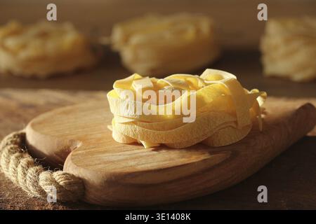Raw italian pasta tagliatelle on wooden cutting board Stock Photo