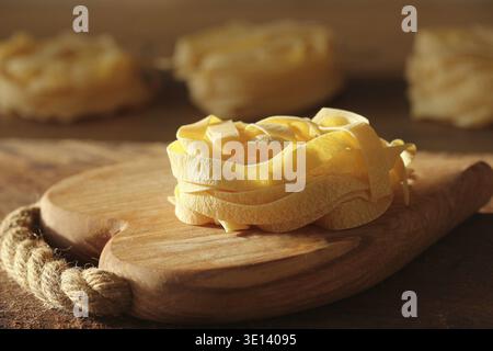 Raw italian pasta tagliatelle on wooden cutting board Stock Photo
