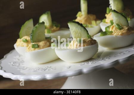 Spicy deviled eggs garnished with cucumber and leek on white plate. Wooden rustic background Stock Photo