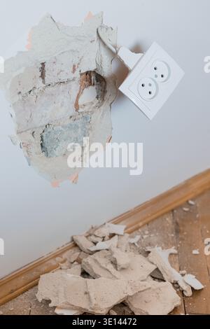 Damaged Wall With Broken Plaster Exposing Brick And Hanging Electrical Outlet Amidst Debris On Wooden Floor In Neutral Tones Stock Photo