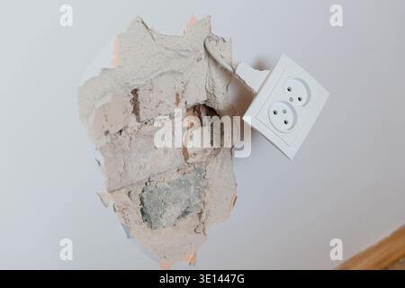 Damaged Wall Exposed Concrete With Detached Electrical Outlet Showing Repair Needs In Neutral Tones Of Gray And White For Construction Concepts Stock Photo