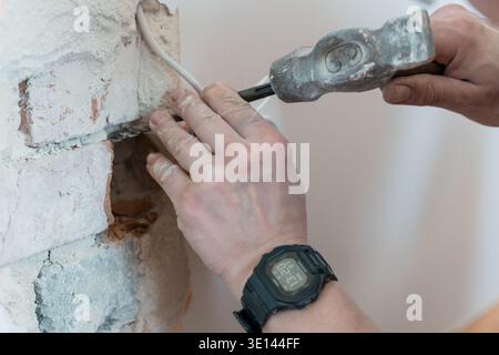 Construction Worker Using Hammer and Chisel on White Brick Wall to Expose Wiring While Wearing Digital Watch During Renovation Project Stock Photo