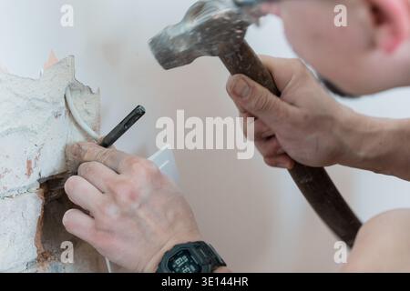 Male Worker Using Hammer And Chisel To Break Concrete Wall With Exposed Wiring In Close-Up Action Shot Featuring Dusty Texture And Realistic Style Stock Photo
