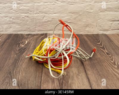 A messy heap of colorful Cat5 ethernet cables in yellow, orange, and white on a wooden floor, conceptualizing IT chaos. Stock Photo