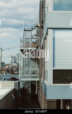 Two staircases lead up the side of a brick building in an urban area. The scene shows grey clouds in the sky with other buildings nearby. Stock Photo