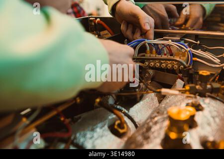 Two people are working inside a workshop. They are repairing and connecting wires to a machine. Tools and equipment are spread around as they focus on Stock Photo