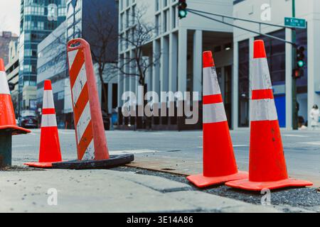 Traffic cones are placed on a street to block off a construction area. Nearby, people walk along the sidewalk. City buildings stand tall in the backgr Stock Photo