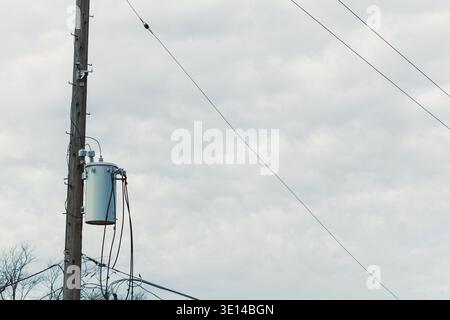 A power transformer is installed on a wooden utility pole. The cloudy sky is above, and power lines stretch out from the pole into the distance. The s Stock Photo