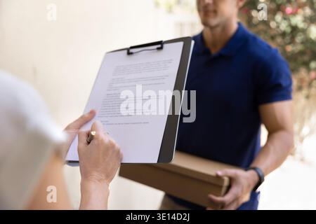 Closeup woman holding clipboard, signing parcel receipt form during delivery Stock Photo