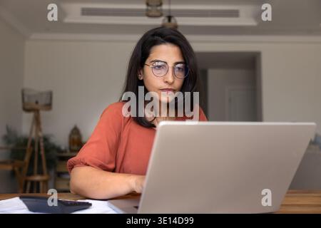 Serious young woman in glasses working on laptop at home Stock Photo