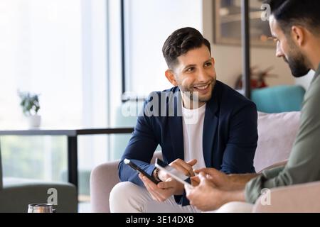 Colleagues holding digital tablet and smartphone, talking during meeting Stock Photo