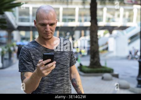 Young handsome bald man using mobile phone outside the mall in the city Stock Photo
