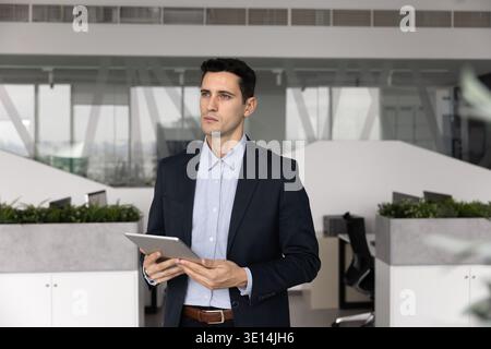 Latin businessman holding tablet thinking about problem solution in office Stock Photo