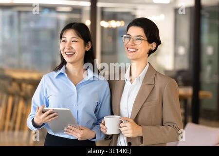 Multiethnic businesswomen, corporate staff members laughing during break in office Stock Photo
