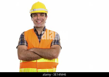 Studio shot of young happy Persian man construction worker smiling with arms crossed Stock Photo