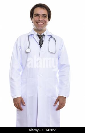Studio shot of young happy Persian man doctor smiling while standing and wearing eyeglasses Stock Photo