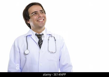 Studio shot of young happy Persian man doctor smiling while thinking Stock Photo