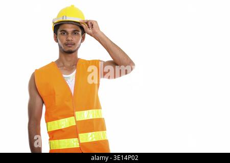Studio shot of young handsome Indian man construction worker holding safety helmet on head Stock Photo
