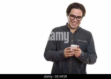 Studio shot of young happy Persian man smiling while using mobile phone Stock Photo