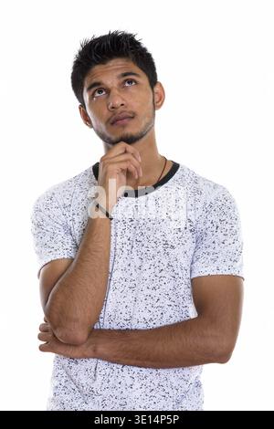 Studio shot of young handsome Indian man thinking while looking up Stock Photo