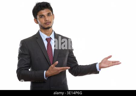 Studio shot of young handsome Indian businessman showing something Stock Photo