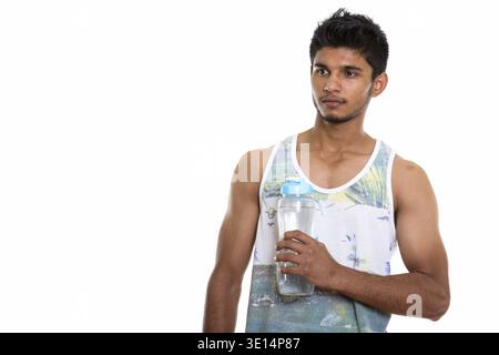 Studio shot of young handsome Indian man holding water bottle and thinking Stock Photo