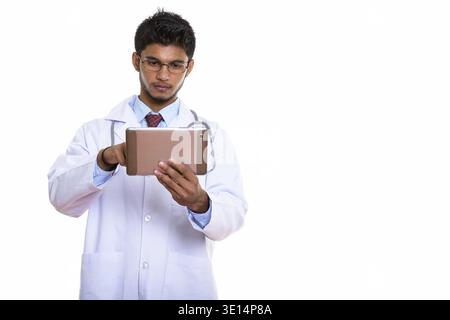 Studio shot of young handsome Indian man doctor using digital tablet Stock Photo