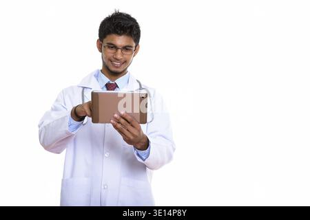 Studio shot of young happy Indian man doctor smiling while using digital tablet Stock Photo