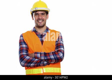 Studio shot of young happy Persian man construction worker smiling with arms crossed Stock Photo