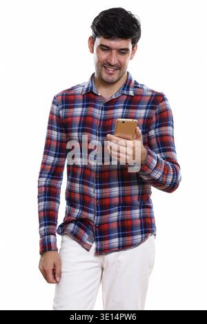 Studio shot of young happy Persian man smiling while using mobile phone Stock Photo
