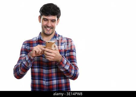 Studio shot of young happy Persian man smiling while using mobile phone Stock Photo