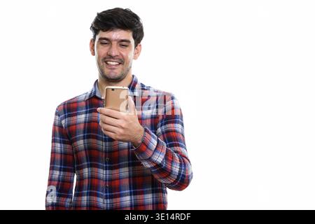 Studio shot of young happy Persian man smiling while using mobile phone Stock Photo