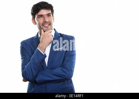 Studio shot of young happy Persian businessman smiling while thinking Stock Photo