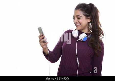 Young happy Indian woman smiling while wearing headphones around neck while using mobile phone Stock Photo