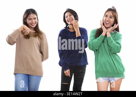 Three happy young Asian woman friends smiling and making funny faces together with one friend pointing finger Stock Photo