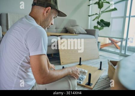 Man focused on assembling flat pack furniture on the floor in a modern apartment Stock Photo