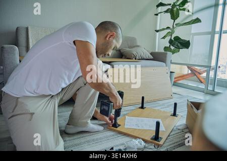 Man installing legs on new flat-pack furniture using a power drill at home Stock Photo