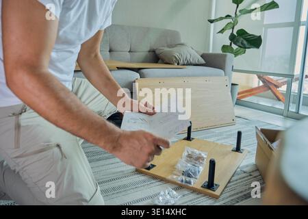 Man reading paper instructions while assembling flat-pack furniture at home Stock Photo