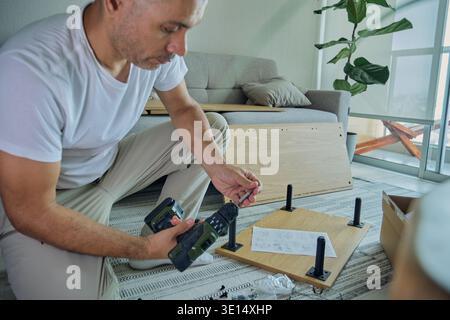 Man building diy furniture at home, using tools and following instructions Stock Photo