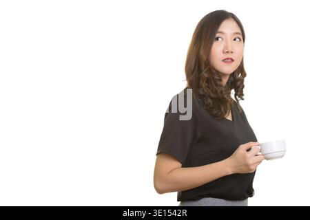 Young beautiful Asian businesswoman holding coffee cup while thinking Stock Photo