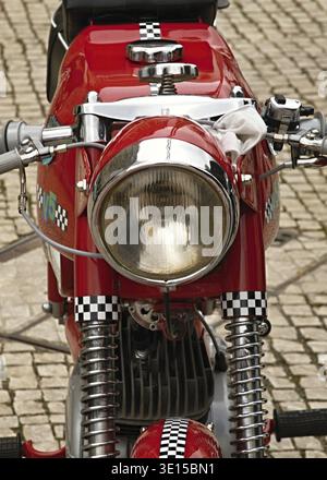Vintage red motorcycle parked on cobblestone street showcasing classic design and details Stock Photo