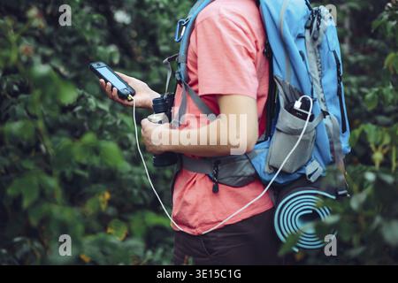 Young man using online maps during the hike, using smart phone, charging mobile phone during the trip, holding backpack Stock Photo