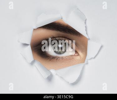 Female eye looking through torn paper Stock Photo