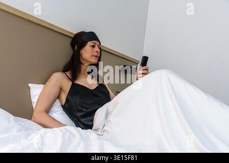 Woman preparing for sleep checking smart remote control Stock Photo