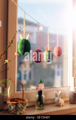 Paper Easter egg decorations hanging against window with sunlight. Selective focus. Stock Photo