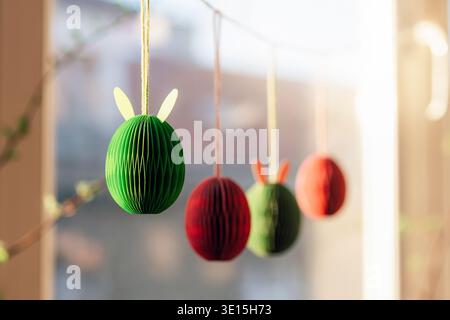 Colorful paper Easter egg decorations hanging by window in sunlight, closeup. Stock Photo