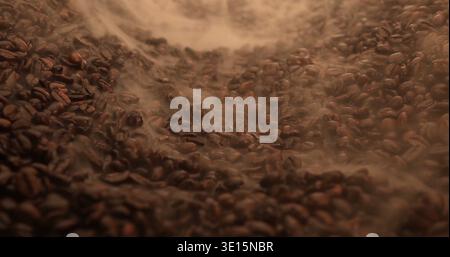 Freshly roasted coffee beans in a dark roasting chamber with smoke rising above them Stock Photo