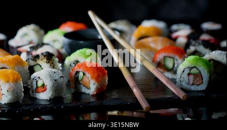 Sushi rolls arranged on a dark surface with chopsticks and soy sauce in a restaurant setting Stock Photo